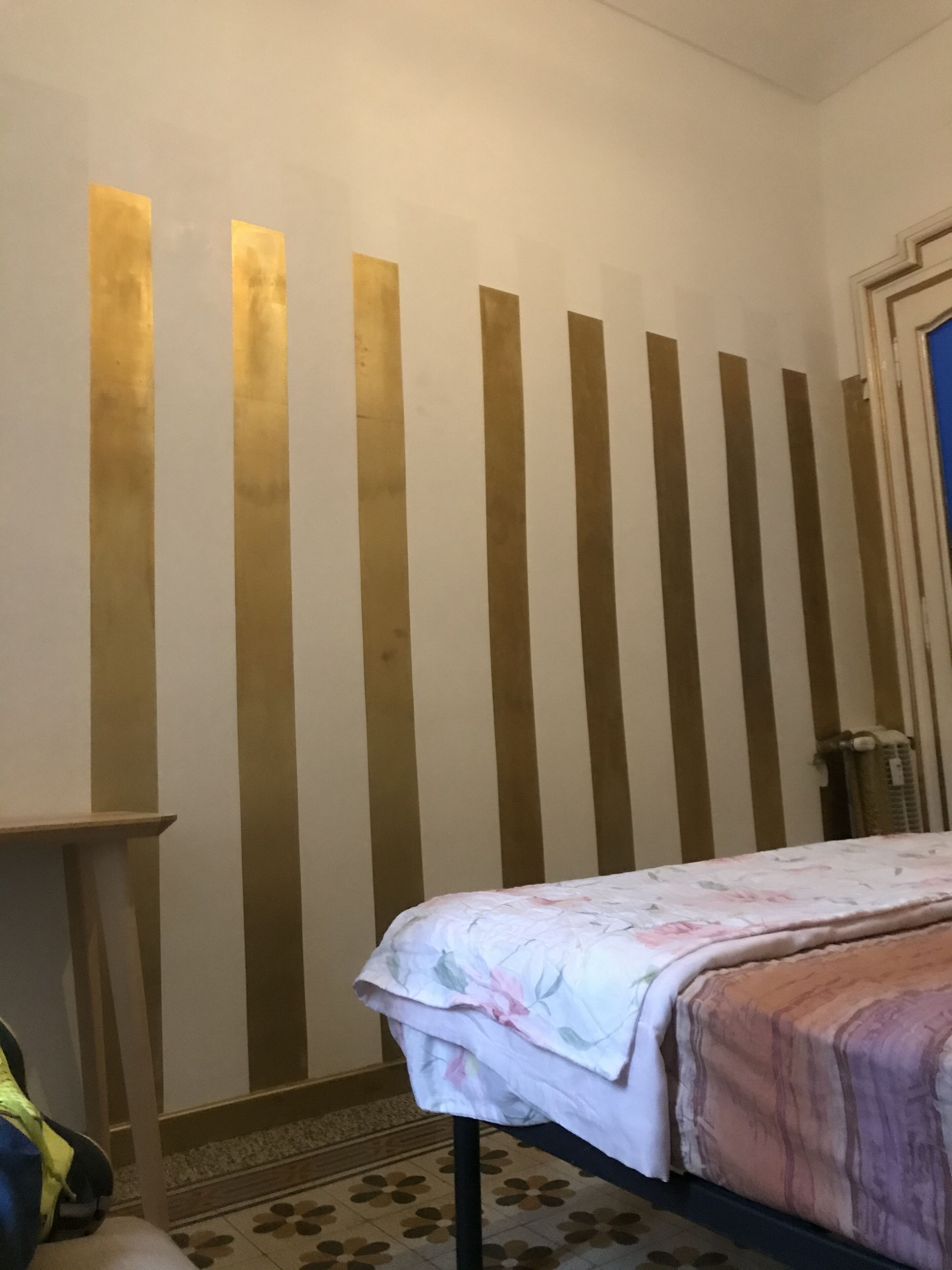 Ein Zimmer mit einem Bett, einem Heizkörper und einer Wand mit vertikalen Streifen.
