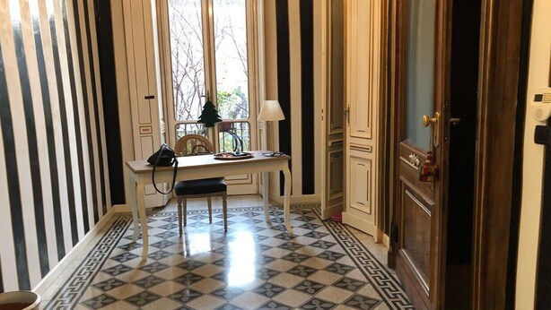 A room with a tiled floor, a table with chairs, a lamp, and a cabinet. - Civico 7 (Turin)
