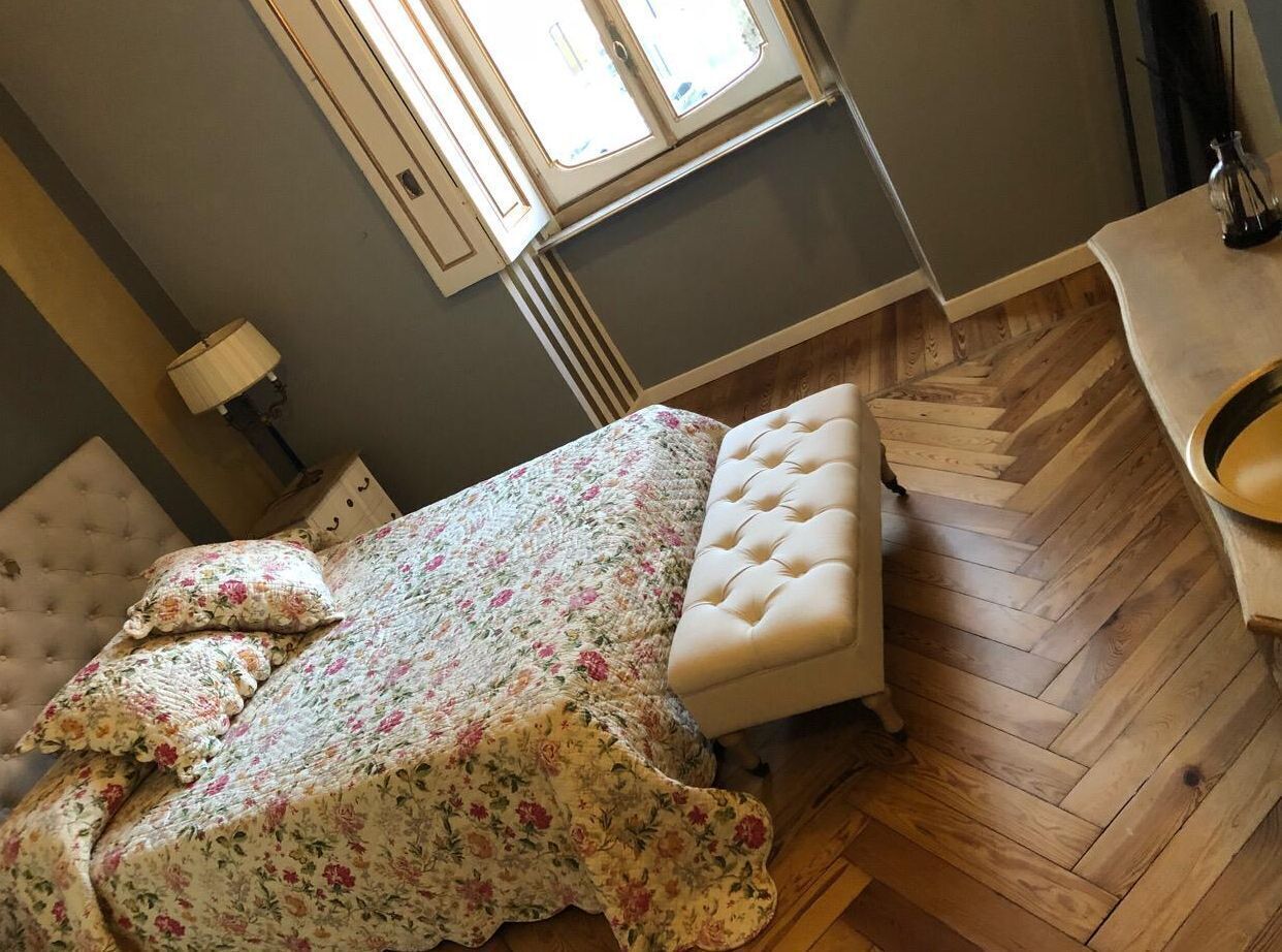 A bedroom with a bed, a bench, a lamp, and a window.