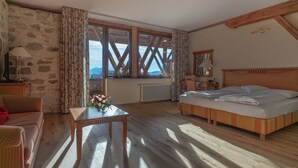 Una habitación con una cama, una mesa con un florero, una silla, un escritorio de madera y una ventana con vista a montañas.
