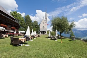 Un espace extérieur aménagé avec des tables et des parasols, une église dotée d’un clocher et une vue sur les montagnes.