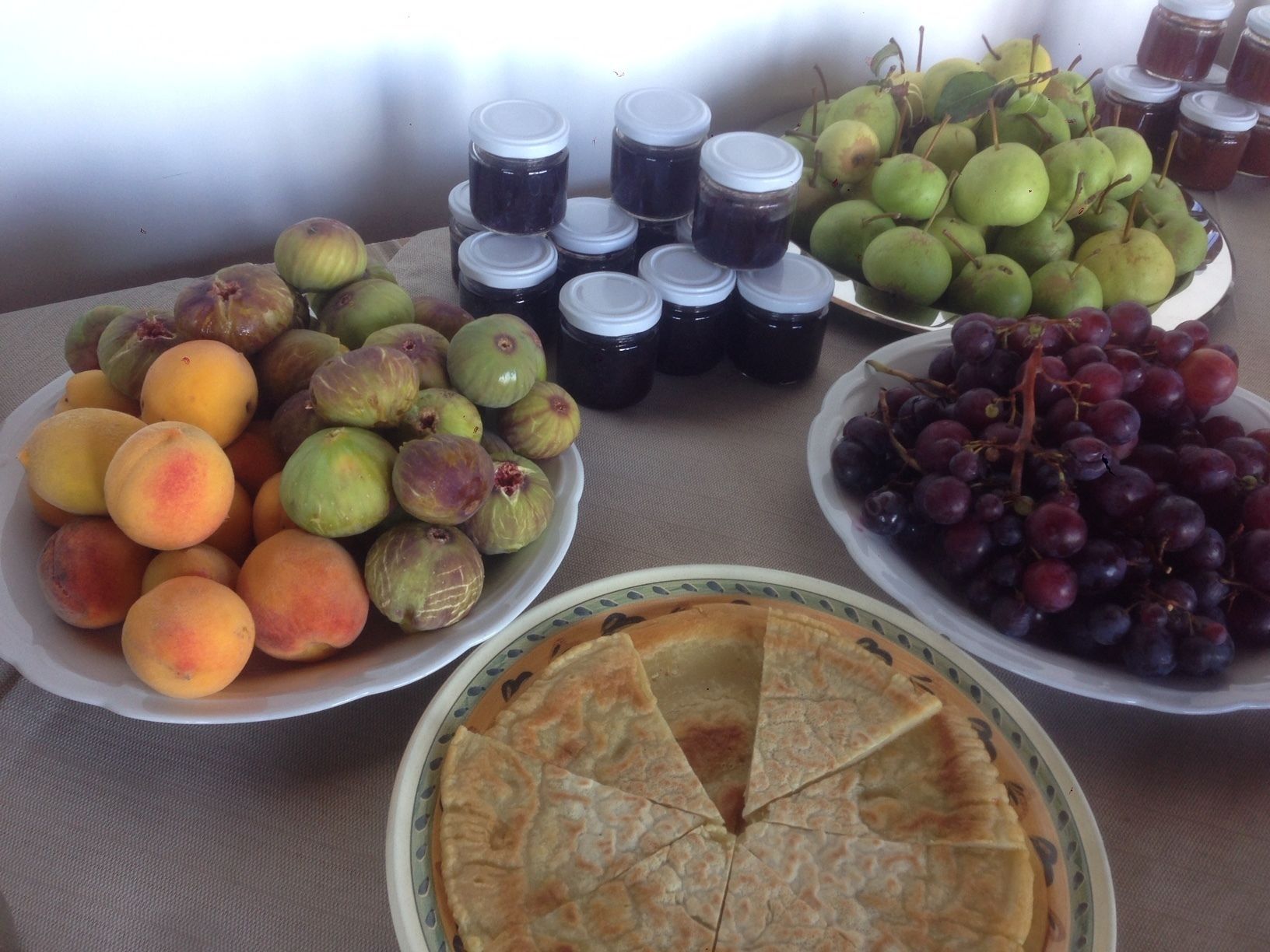 Une table garnie de divers fruits, de pots de confitures et d’une tarte.