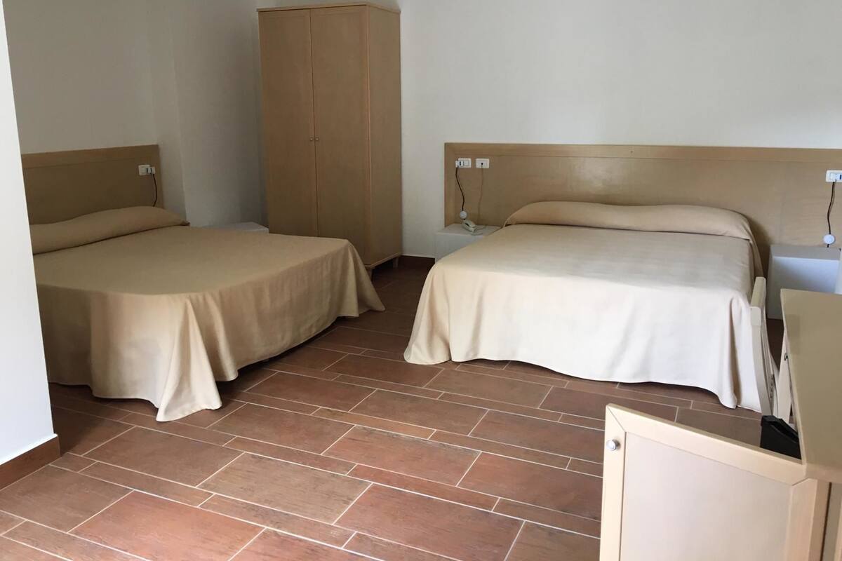 A room with two beds, a wardrobe, a bedside table with a lamp, and a small desk.