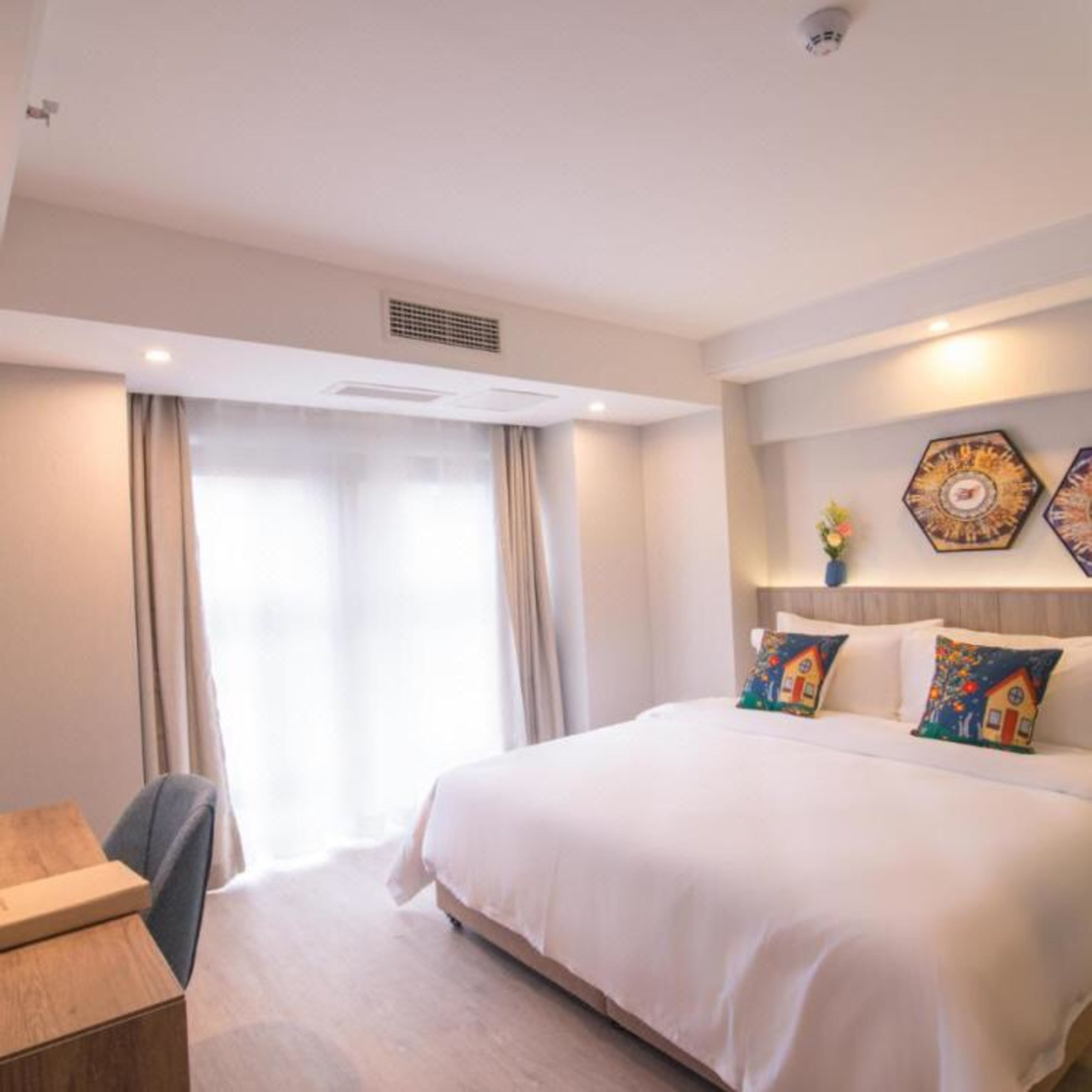 A hotel room with a large bed, a desk, and a window with curtains.