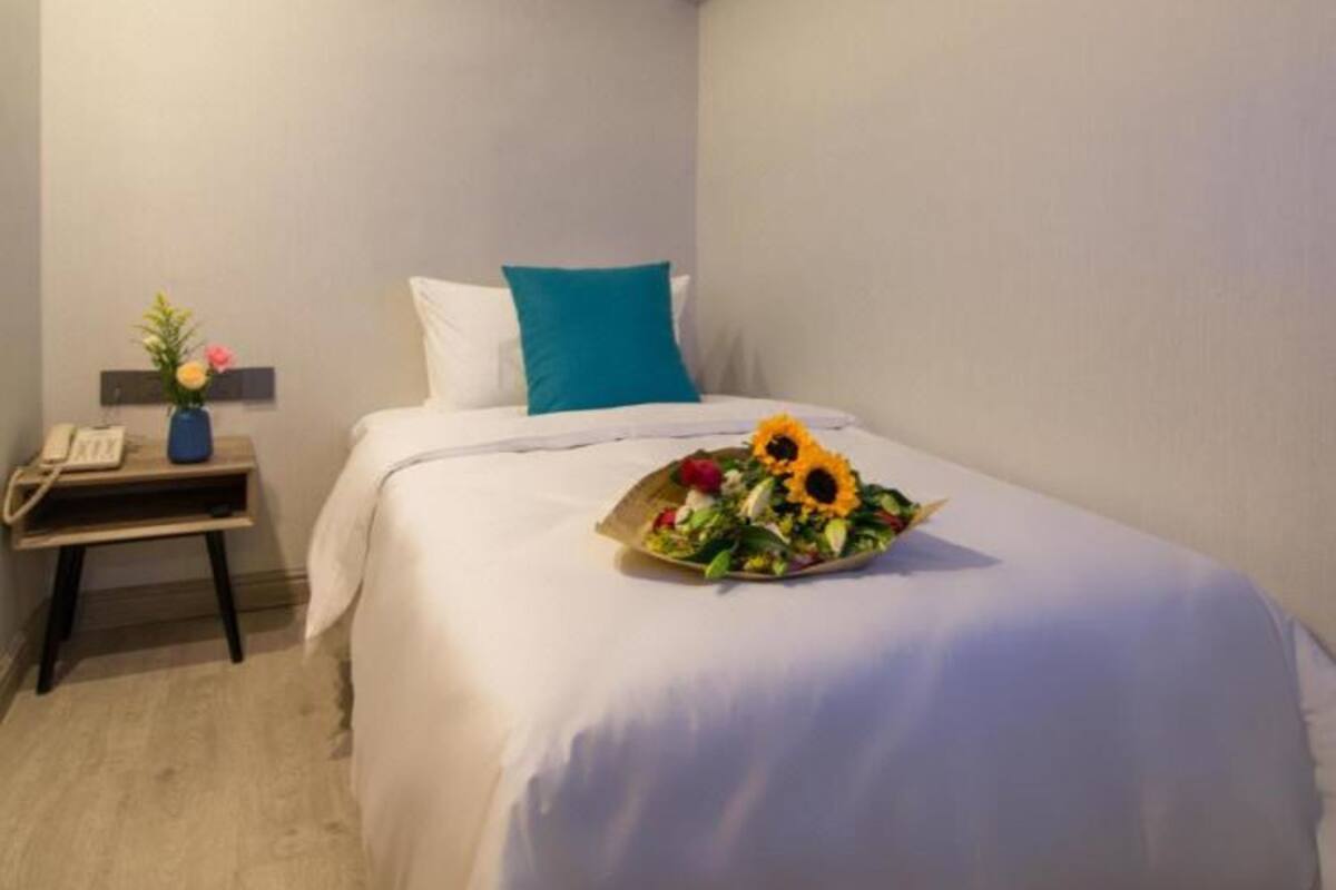 Ein Hotelzimmer mit Bett, Nachttisch, einer Vase mit Blumen und einem Sonnenblumenstrauß auf dem Bett.