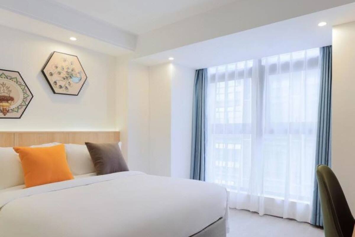 Ein Hotelzimmer mit einem großen Bett, einem Holz-Kopfteil, zwei sechseckigen Wandbildern, einem Fenster mit blauen Vorhängen und einem grünen Sessel.