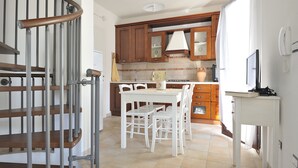 A kitchen with wooden cabinets, a white table, and chairs. - Residence Bianco Navarrese A (Baunei)