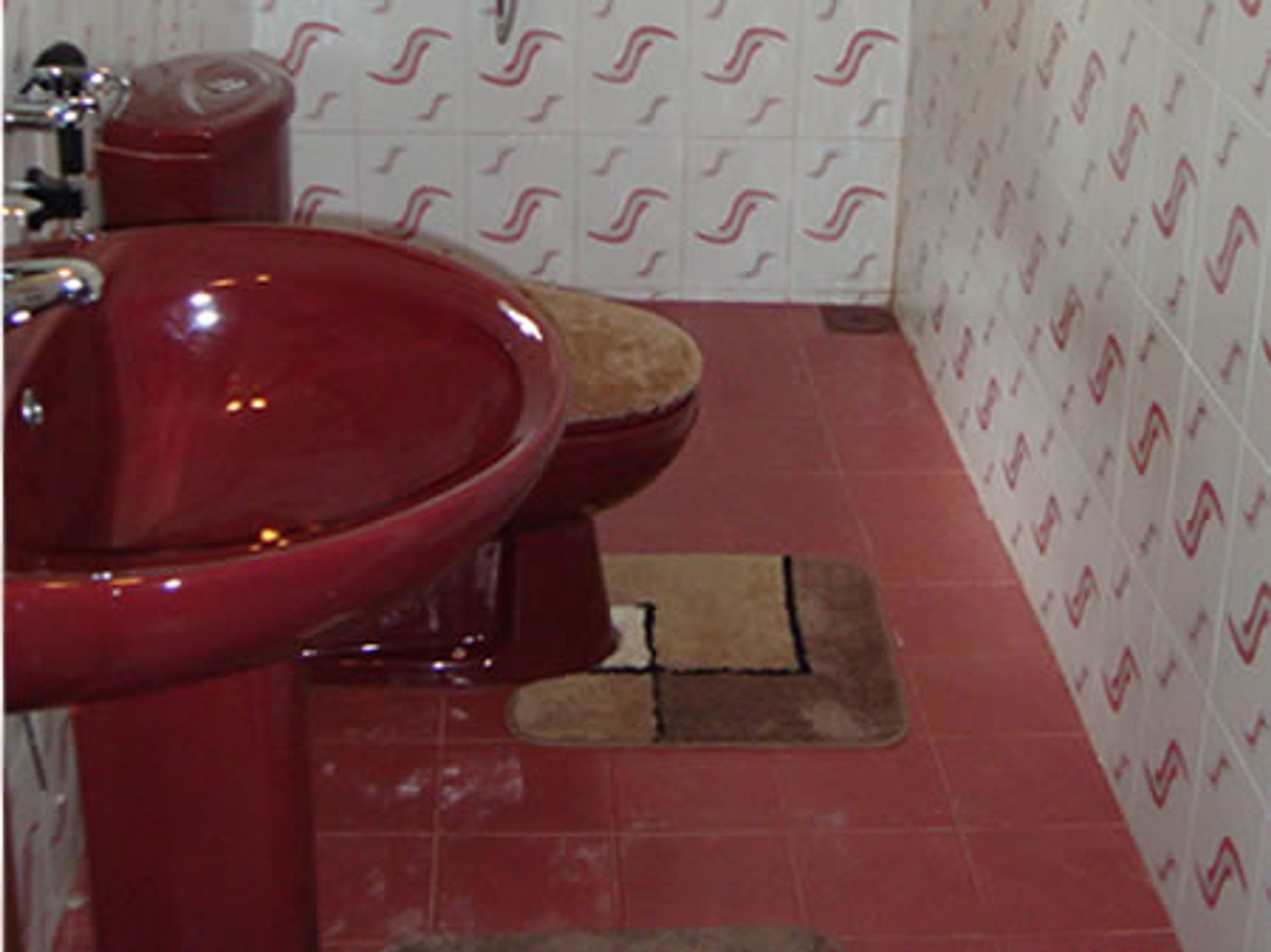 Une salle de bain avec un lavabo rouge, des toilettes et des carreaux blancs à motifs sur les murs et le sol.