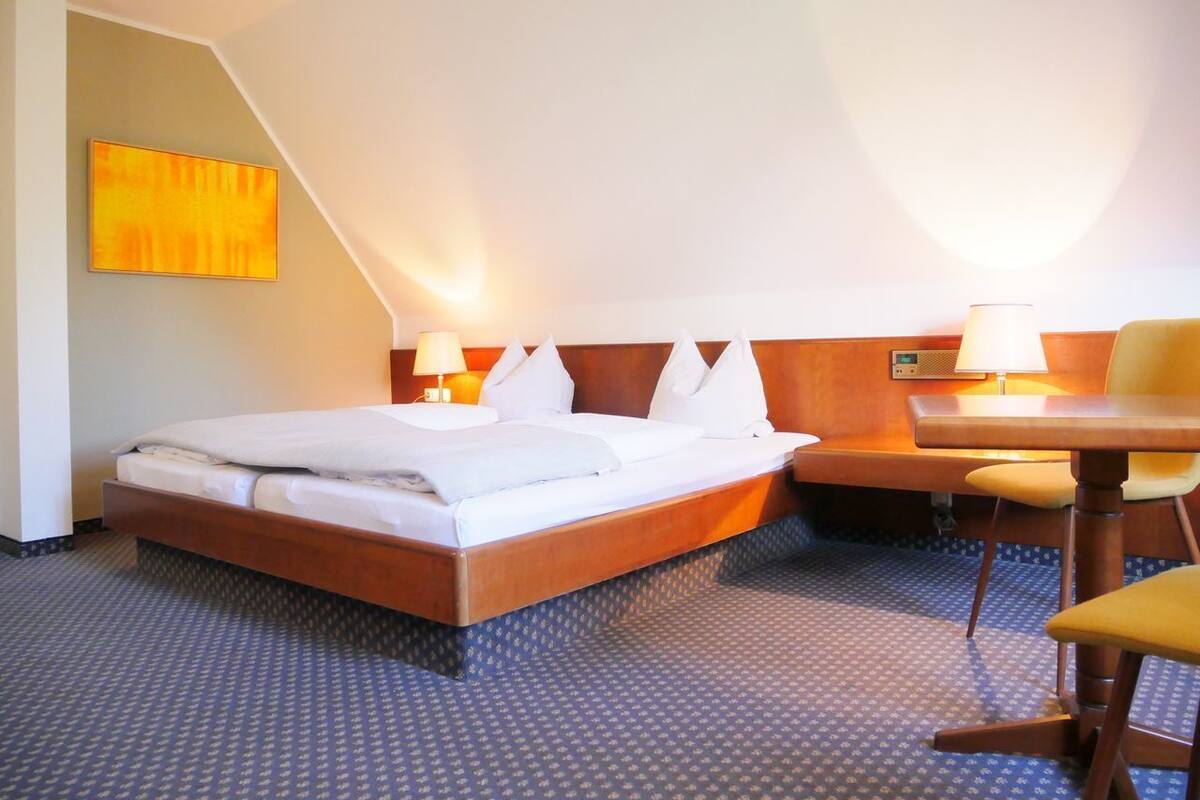 A hotel room with a bed, bedside tables, a chair, and a wall-mounted lamp.