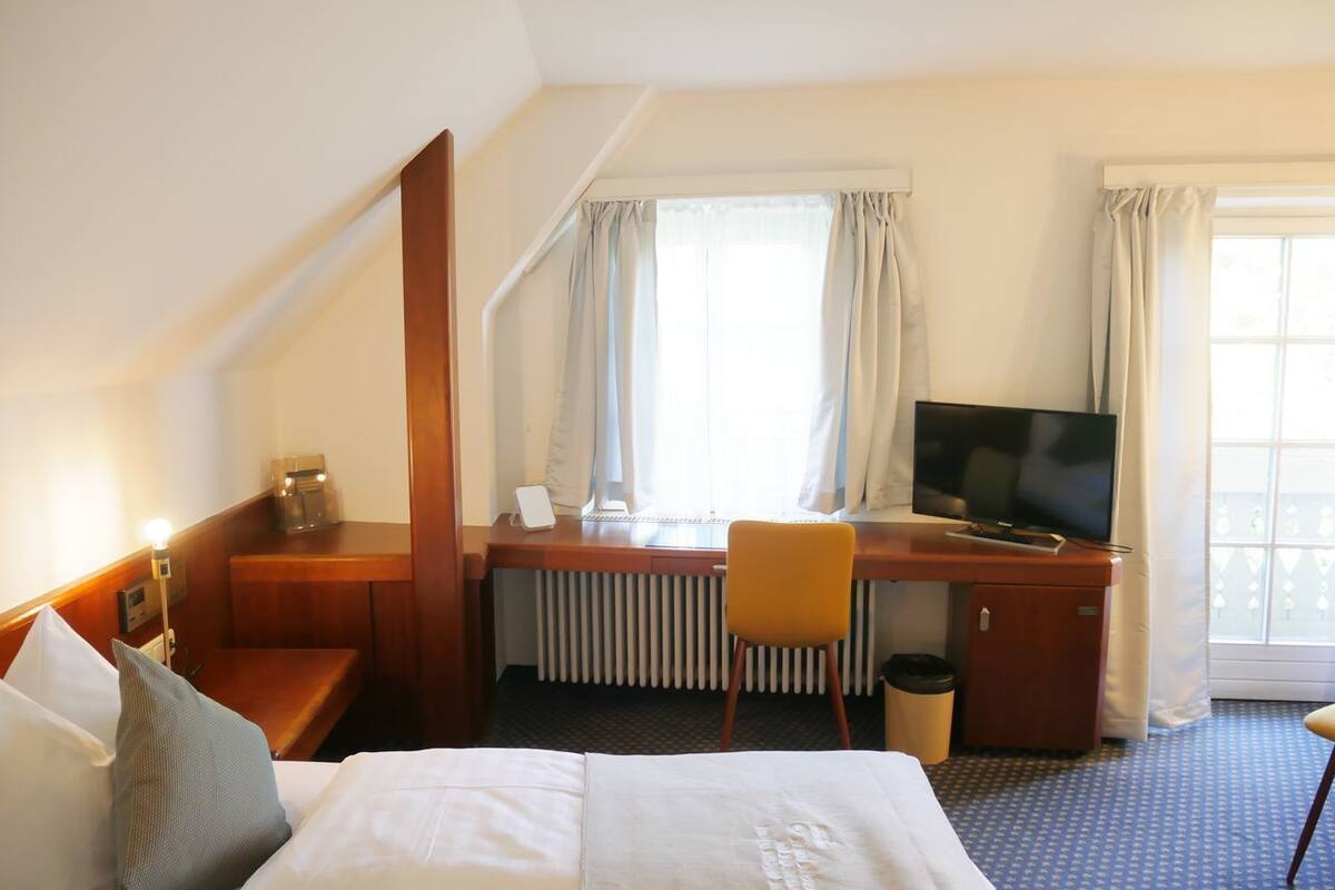 A hotel room with a bed, a desk with a computer, a television, and a window with curtains.