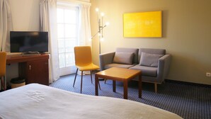Een hotelkamer met een bed, een bureau met een televisie, een bank, een stoel en een vloerlamp.