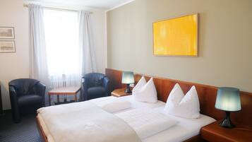 A hotel room with a large bed, two bedside tables, a small table, two chairs, and a window with curtains.
