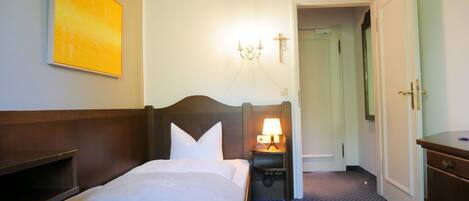 A hotel room with a bed, bedside table, lamp, and a painting on the wall.