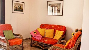 A room with wicker furniture, a red sofa with colorful cushions, and two framed pictures on the walls. - Residence Bianco Navarrese B (Baunei)