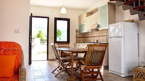 A compact kitchen with a dining table and chairs, a refrigerator, and a staircase leading to an upper level. - Residence Bianco Navarrese B (Baunei)