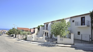 A residential street with white houses, a clear sky, and a tree in the foreground. - Residence Bianco Navarrese B (Baunei)