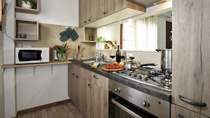 A modern kitchen with wooden cabinets, a microwave, a stove, and various kitchen items on the counter. - Casa di Zio Mario A (Baunei)