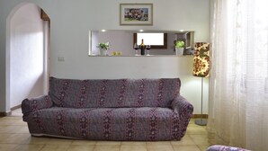 A living room with a patterned sofa, a small table with decorative items, a floor lamp, and a framed picture on the wall. - Casa di Zio Mario A (Baunei)