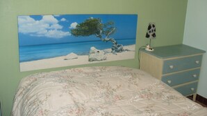 Een slaapkamer met een bed, een kaptafel, een schilderij van een strandtafereel en een lamp.