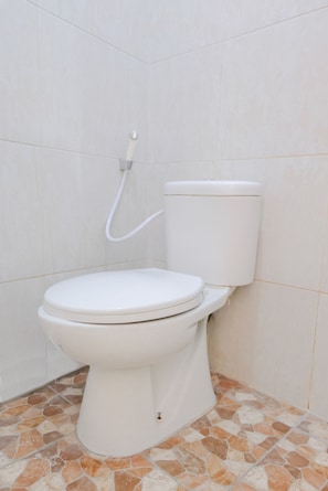 Inodoro blanco con tanque y un accesorio bidé en un baño con paredes de azulejos y suelo de mosaicos.