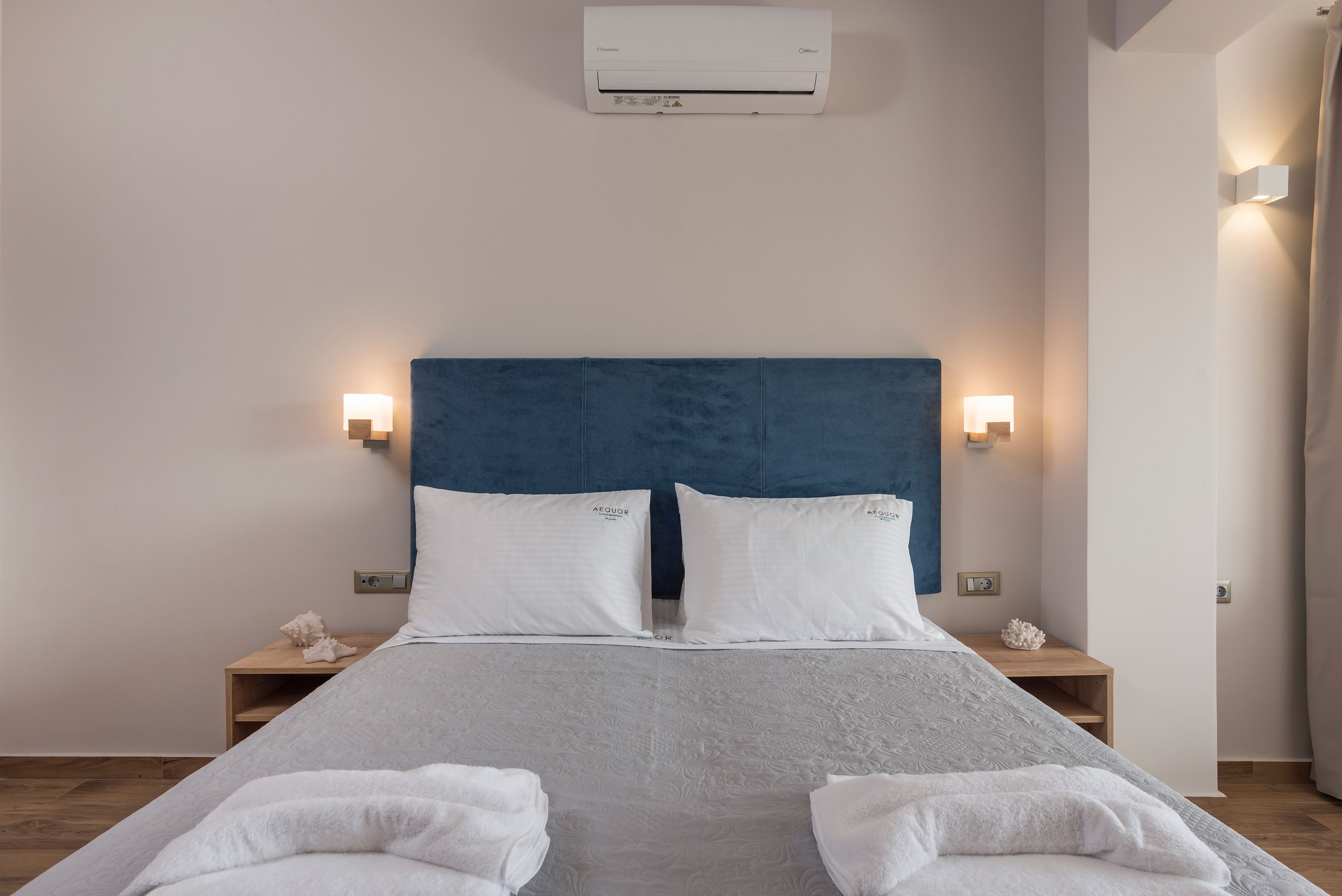 A neatly made bed with white linens, a blue headboard, and two bedside tables with lamps.