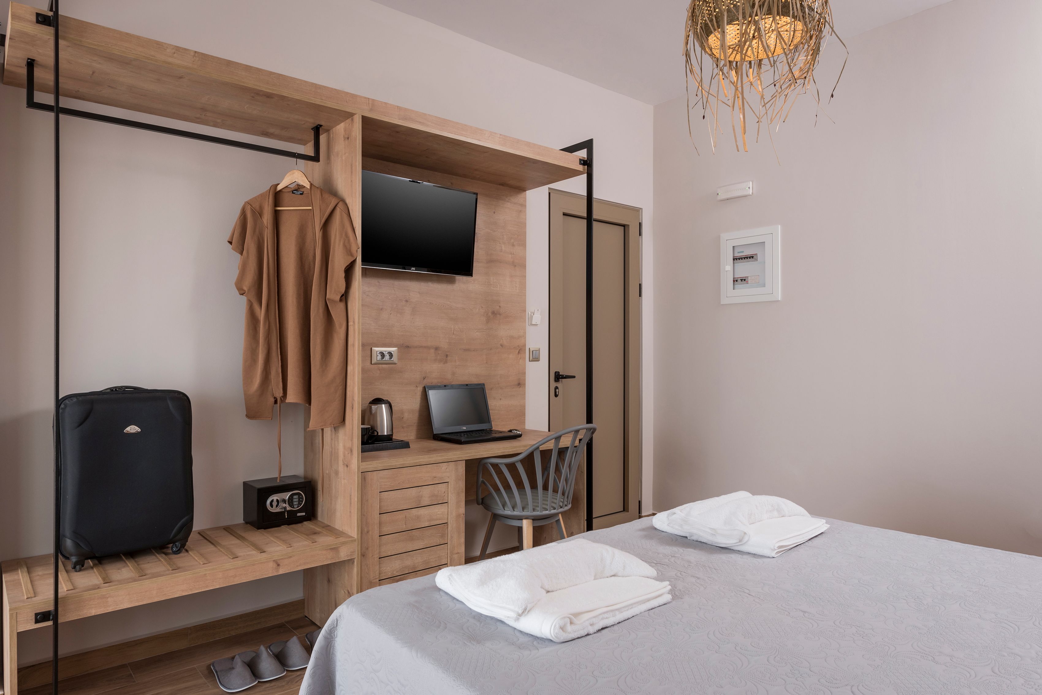 Ein Hotelzimmer mit Bett, Schreibtisch mit Laptop, Stuhl, an der Wand montiertem Fernseher und Koffer auf dem Boden.