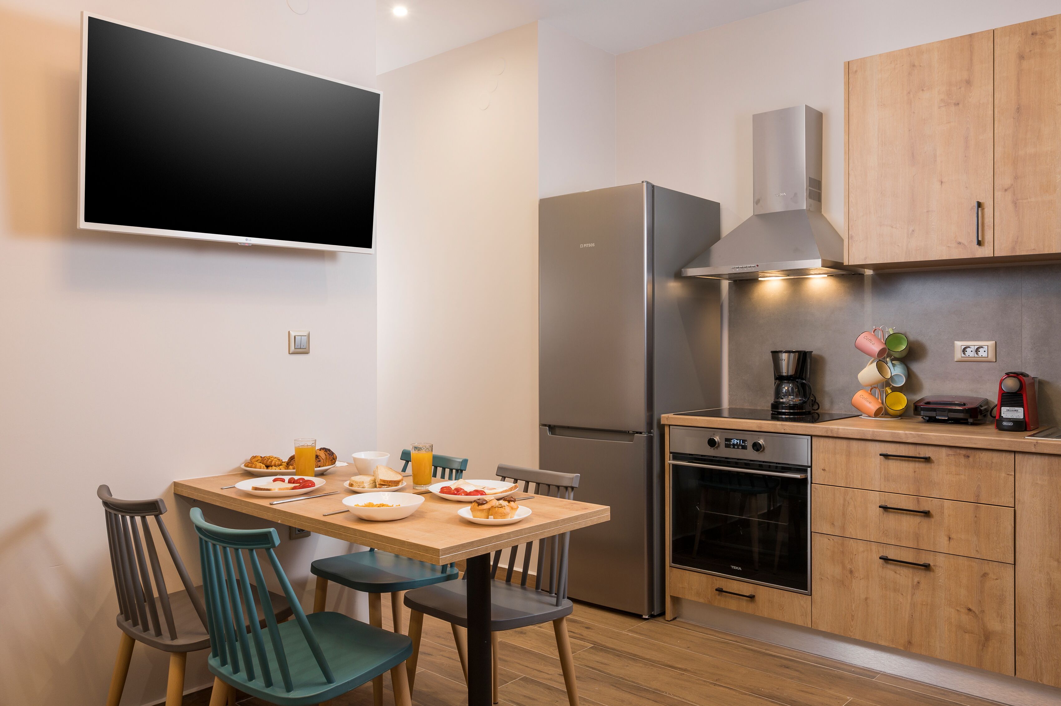 Une cuisine moderne équipée d’un téléviseur à écran plat, d’un réfrigérateur en acier inoxydable, de meubles de rangement en bois et d’une table à manger avec des chaises.
