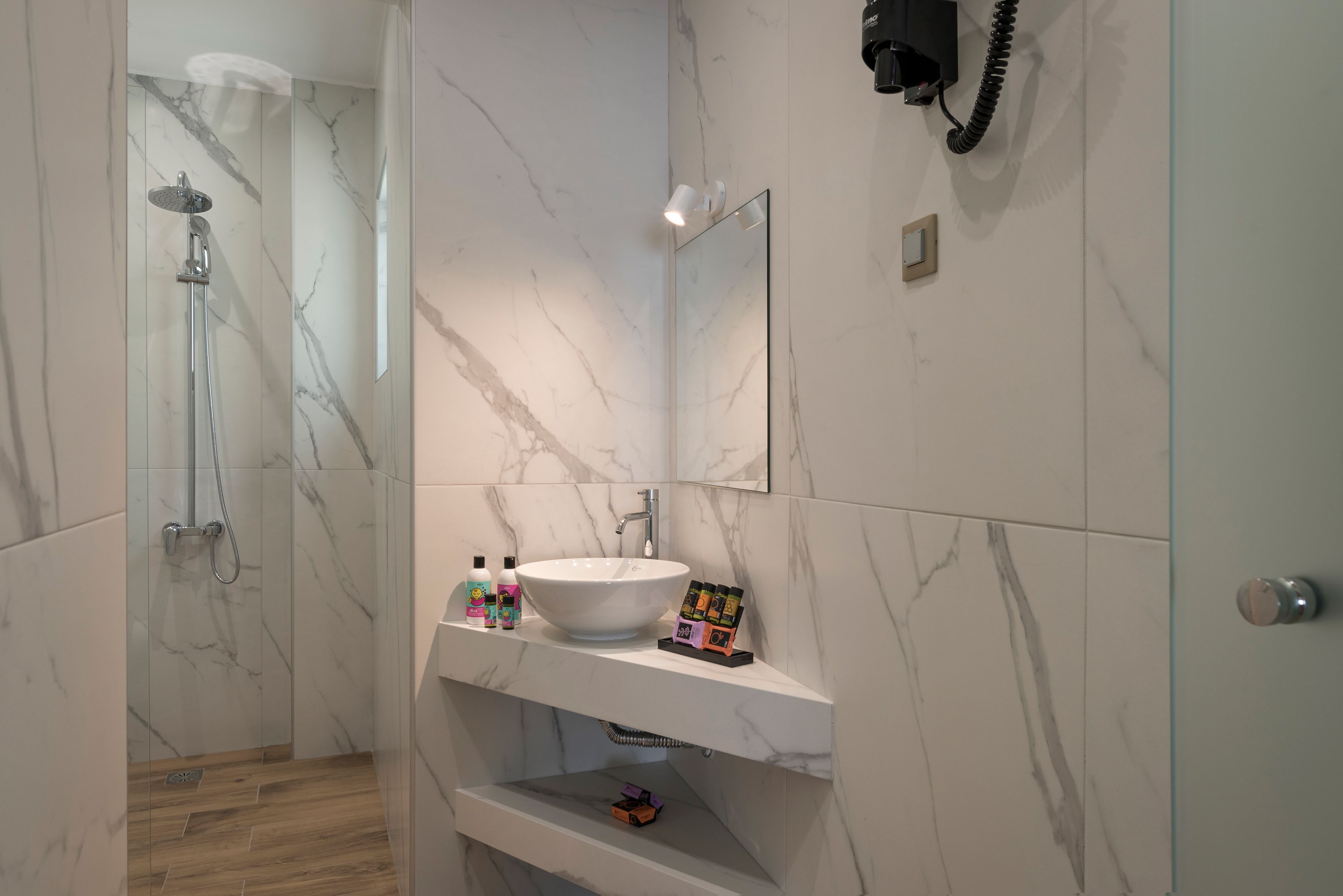 A modern bathroom with a marble wall, a white sink, a handheld showerhead, and a mounted phone.