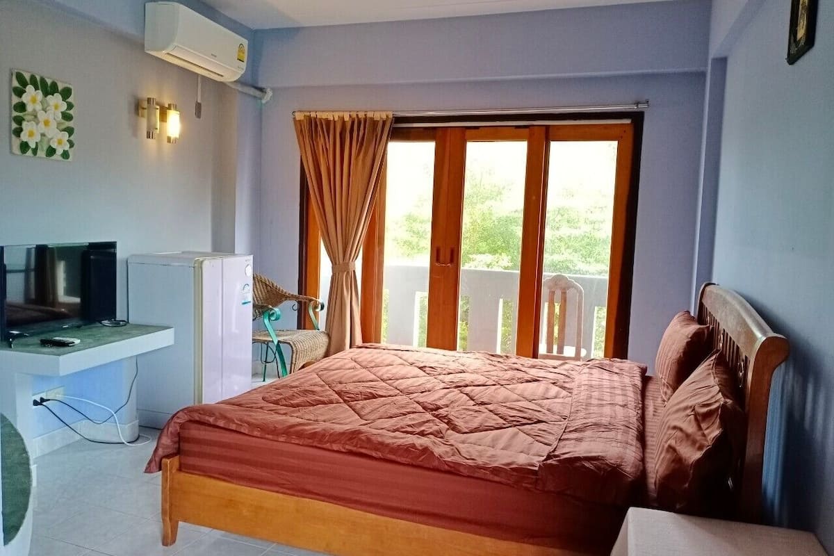 A bedroom with a bed, a desk, a chair, an air conditioner, and a window with curtains.