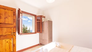 A bedroom with a large wooden wardrobe, a window with a view of greenery, and a bed with rolled towels. - Dommu Ala (Baunei)