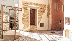 A narrow cobblestone street with a stone building featuring a wooden door and a small window. - Dommu Ala (Baunei)