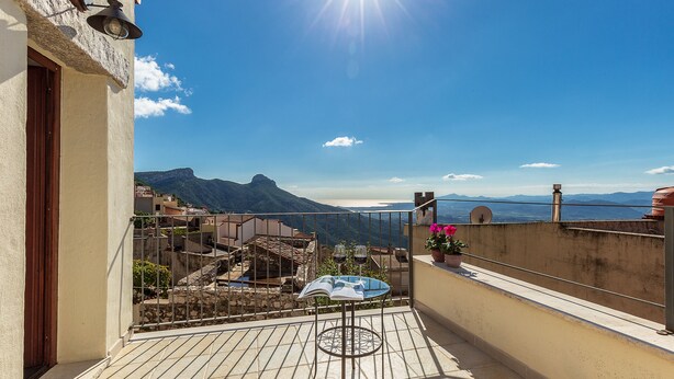 A balcony with a table and chairs, a potted plant, and a view of a mountainous landscape. - Dommu Ala (Baunei)