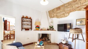 A living room with a fireplace, a television, a sofa, and a dining area in the background. - Dommu Ala (Baunei)