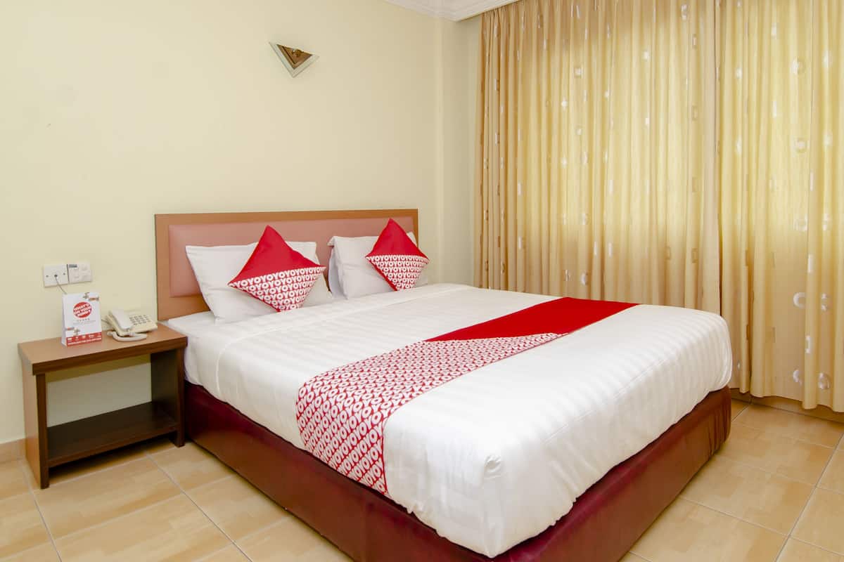 A hotel room with a large bed, a wooden nightstand, a telephone, and a curtain.
