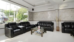 A modern reception area with black leather sofas, a glass coffee table, and a large window offering a view of the street. - Halim Hotel (Tanjung Pinang)