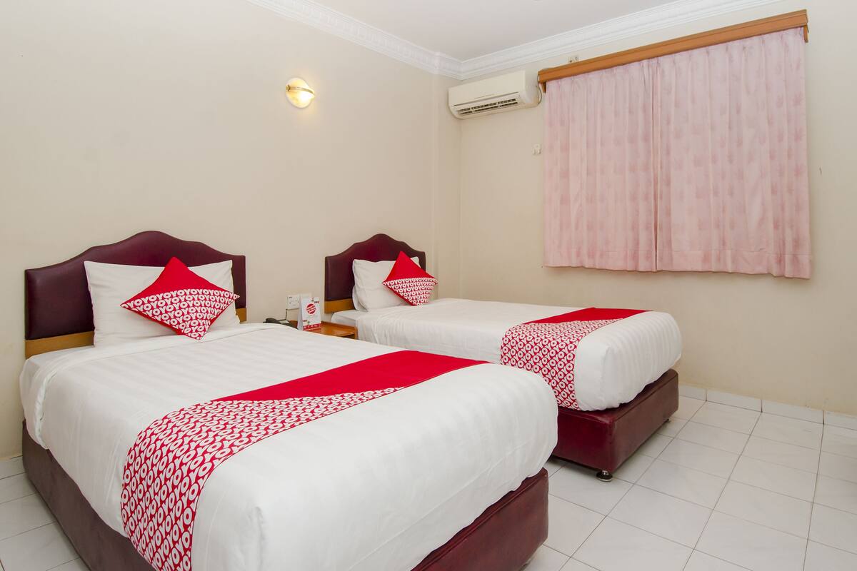 A hotel room with two beds, each with a red and white patterned bedspread, a wooden headboard, and a nightstand with a lamp.