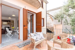 An open-plan living area with a dining table and chairs, a wicker sofa with cushions, and a staircase leading to an upper level. - Casa Goloritzè (Baunei)