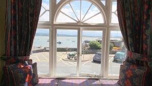A room with a large bay window overlooking a harbor with boats and a motorcycle parked outside. - Dovey Inn (Aberdovey)