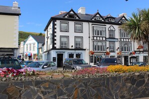 A traditional building with a sign 'DOVEY INN' indicating a hotel. There are parked cars in front, and a stone wall with flowers in the foreground. - Dovey Inn (Aberdovey)