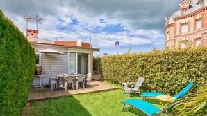 Un jardín bien cuidado con un patio, mobiliario exterior y un seto.