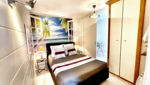 Un dormitorio con cama, mesita de noche, lámpara, armario y vista al océano a través de una ventana.