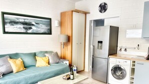 Un espacio habitable compacto con kitchenette, lavadora, mesa de comedor y sofá con cojines.