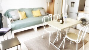 Un espacio habitable compacto con sofá, mesa de comedor, sillas, lavadora y televisor.