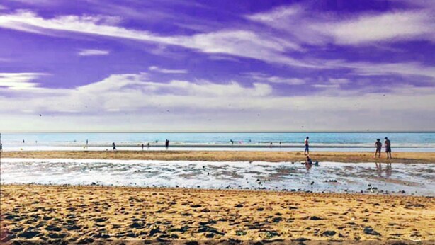 Una playa con gente caminando y parada sobre la arena, y el océano al fondo.