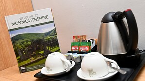 Una bandeja con un libro titulado 'Welcome to Monmouthshire', un hervidor, tazas de té y bolsitas de té galés.
