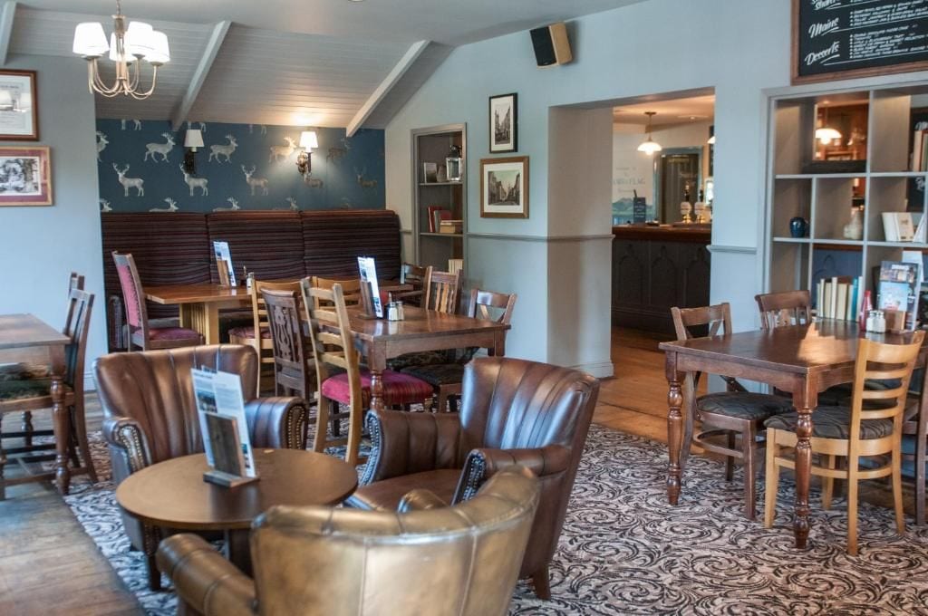 A cozy restaurant with wooden tables and leather chairs, a bar area, and a bookshelf with various items.
