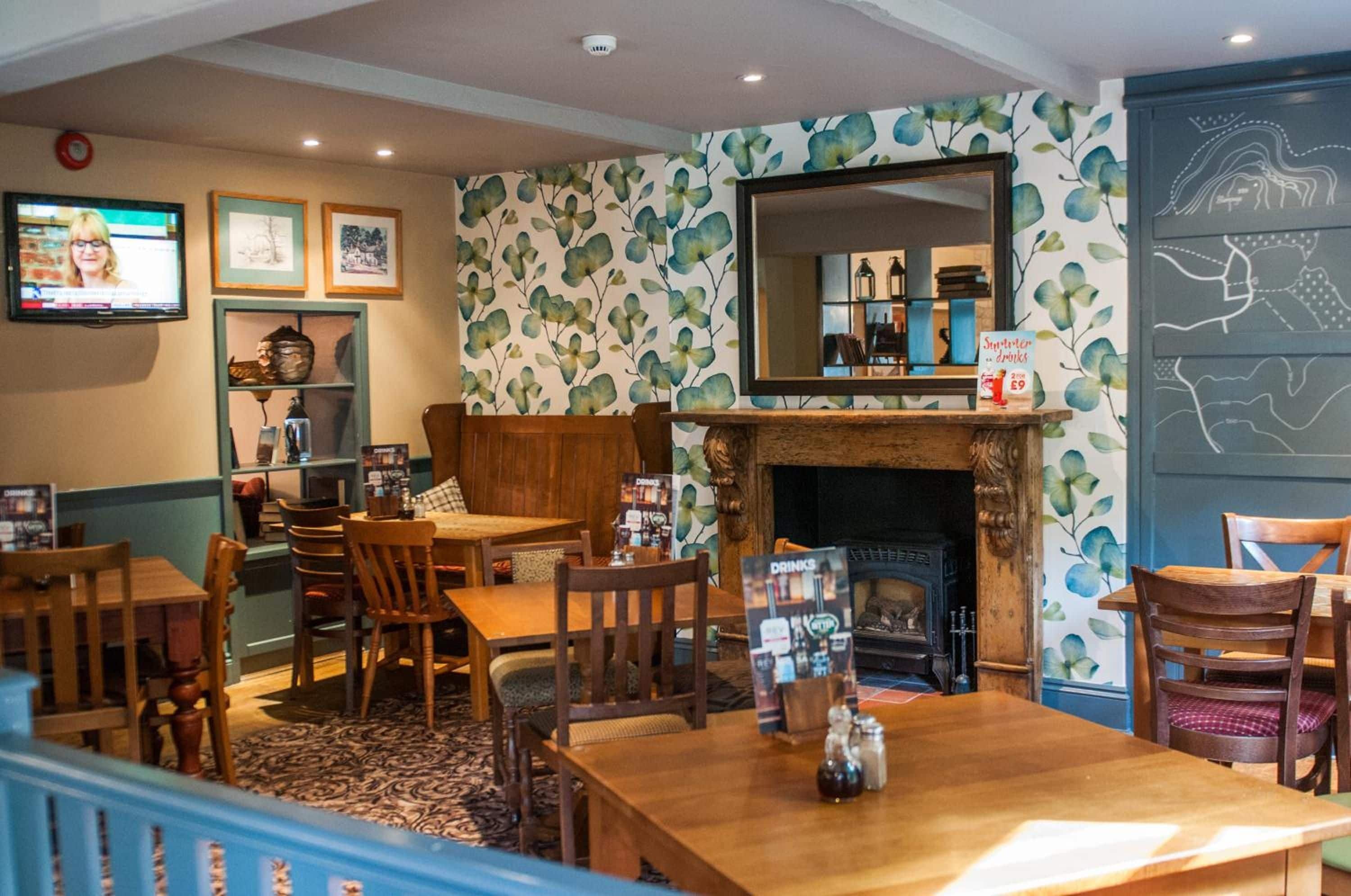 A cozy restaurant interior with wooden furniture, a fireplace, and a wall-mounted television.