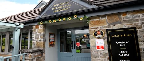 A stone building with a sign reading "Welcome to the Lamb & Flag Abergavenny."