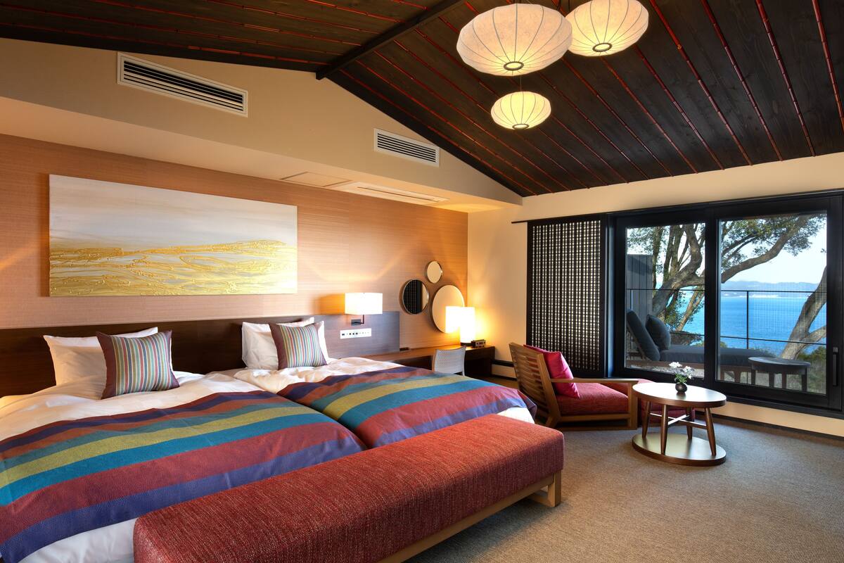 A hotel room with a large bed, a small round table, a chair, and a view of the sea.