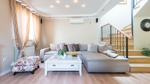 A modern living room with a sofa, ottoman, and coffee table, a staircase with a railing, and an air conditioning unit on the wall. - Vacation house Cavtat (Konavle)